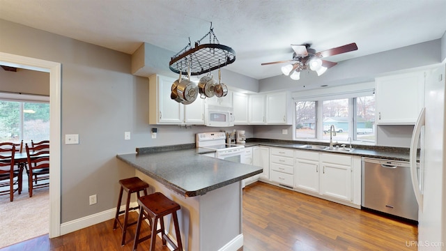 kitchen featuring kitchen peninsula, dark hardwood / wood-style flooring, white appliances, sink, and white cabinets