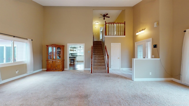 unfurnished living room with ceiling fan, a towering ceiling, and light colored carpet