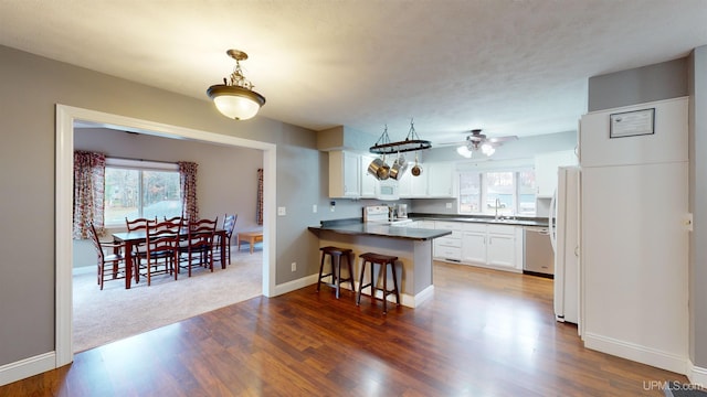 kitchen with kitchen peninsula, a kitchen bar, white appliances, white cabinets, and dark hardwood / wood-style floors