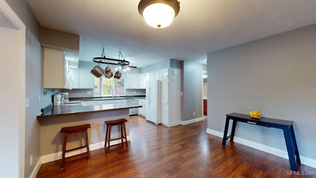 kitchen with white cabinets, a kitchen breakfast bar, appliances with stainless steel finishes, dark hardwood / wood-style flooring, and kitchen peninsula