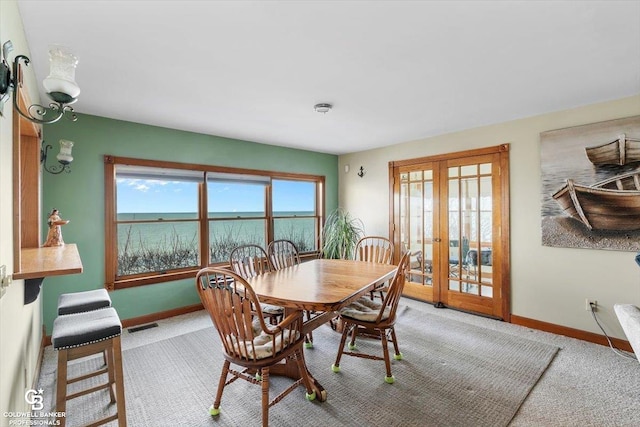 dining area with carpet, a water view, and french doors