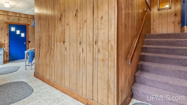 stairway featuring wooden walls and a drop ceiling