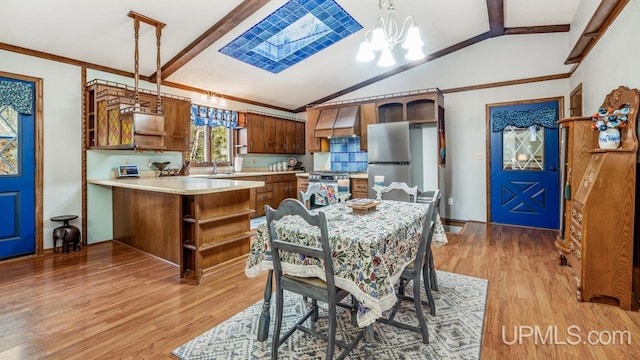 dining space featuring a chandelier, light hardwood / wood-style floors, lofted ceiling with skylight, and sink