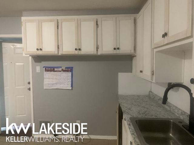 kitchen featuring white cabinets, light stone countertops, and sink