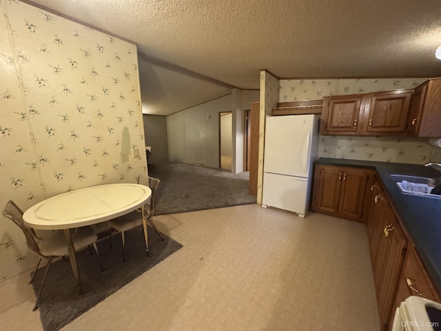 kitchen with a textured ceiling, white refrigerator, and sink