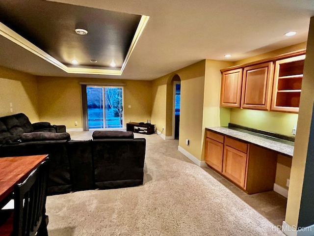 home theater featuring a tray ceiling, light carpet, and built in desk