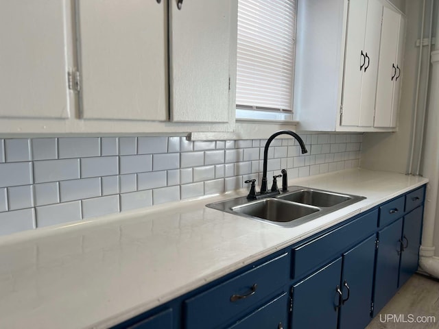 kitchen featuring blue cabinetry, decorative backsplash, white cabinetry, and sink