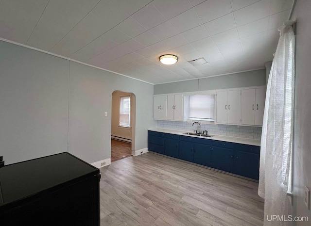 kitchen featuring blue cabinets, sink, light hardwood / wood-style flooring, decorative backsplash, and white cabinetry