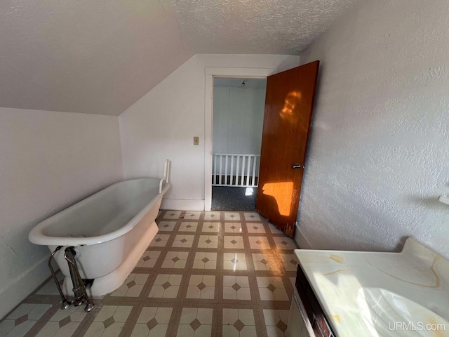 bathroom featuring a textured ceiling, vanity, a bath, and vaulted ceiling