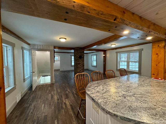 kitchen with dark hardwood / wood-style floors, beam ceiling, a kitchen bar, and light stone counters