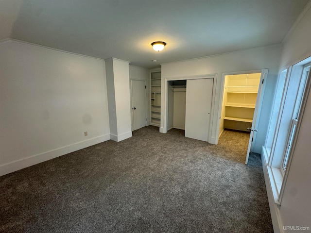 unfurnished bedroom with dark carpet, a spacious closet, and crown molding