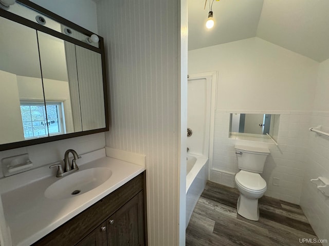 full bathroom featuring wood-type flooring, vaulted ceiling, toilet, vanity, and tile walls