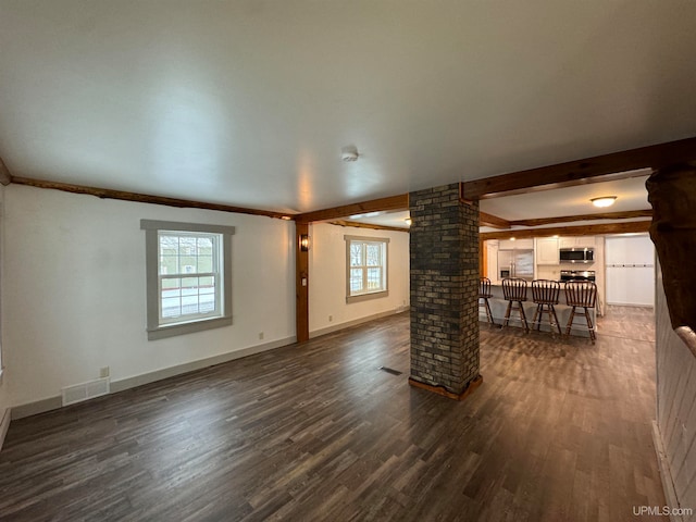 unfurnished living room featuring plenty of natural light, dark hardwood / wood-style floors, ornate columns, and crown molding