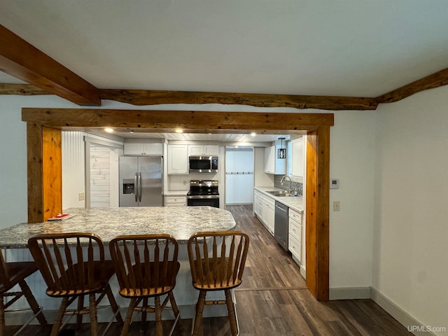 kitchen featuring kitchen peninsula, appliances with stainless steel finishes, a kitchen breakfast bar, dark wood-type flooring, and white cabinetry