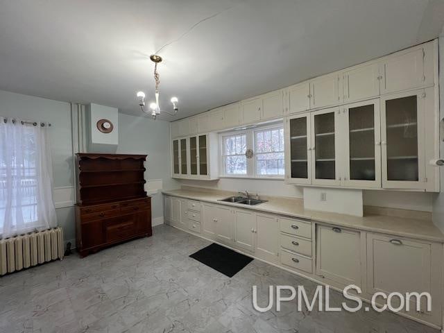 kitchen featuring radiator, sink, a notable chandelier, white cabinetry, and hanging light fixtures