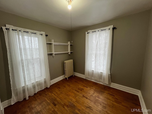 empty room with radiator heating unit and dark hardwood / wood-style flooring