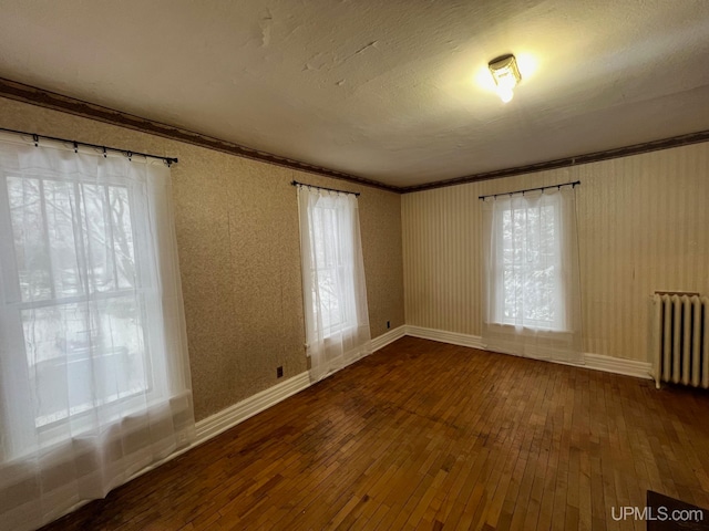 unfurnished room featuring hardwood / wood-style floors, a wealth of natural light, ornamental molding, and radiator