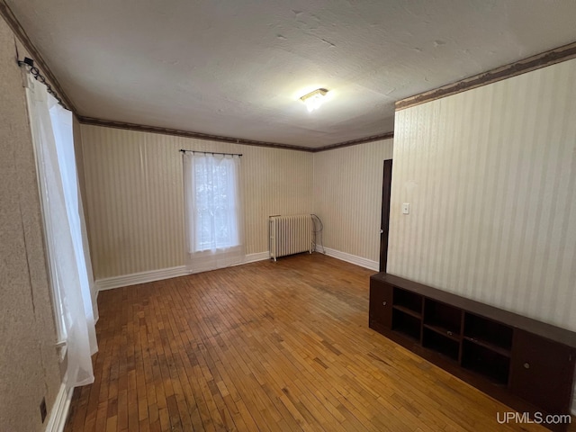 empty room with hardwood / wood-style flooring, radiator, and ornamental molding