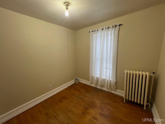 spare room featuring dark hardwood / wood-style flooring and radiator