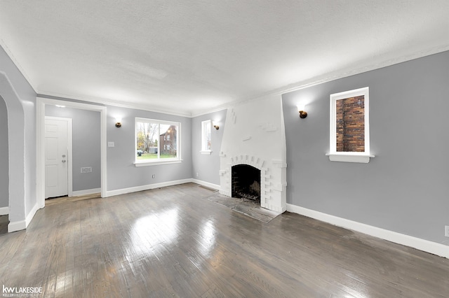 unfurnished living room featuring crown molding, dark wood-type flooring, a textured ceiling, and a brick fireplace