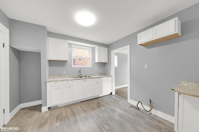 kitchen with white cabinets, light hardwood / wood-style floors, light stone counters, and sink