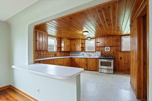 kitchen featuring kitchen peninsula, decorative backsplash, wooden walls, and stainless steel range with gas stovetop