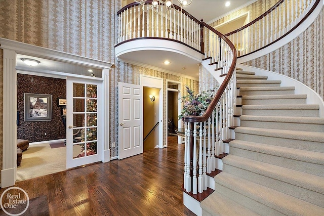 entryway with french doors, crown molding, a towering ceiling, wood finished floors, and wallpapered walls