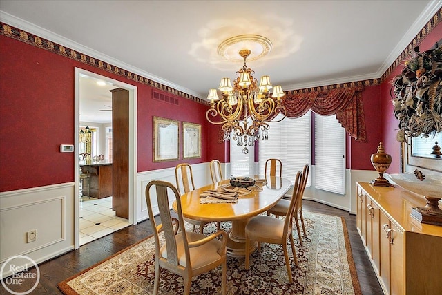 dining area with crown molding, visible vents, dark wood-type flooring, wainscoting, and a chandelier