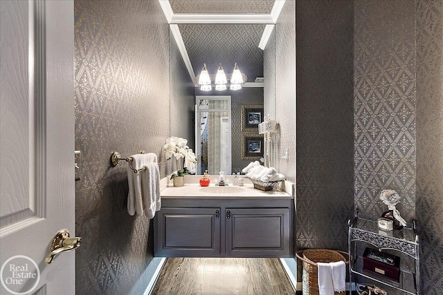 bathroom featuring baseboards, wood finished floors, vanity, and wallpapered walls