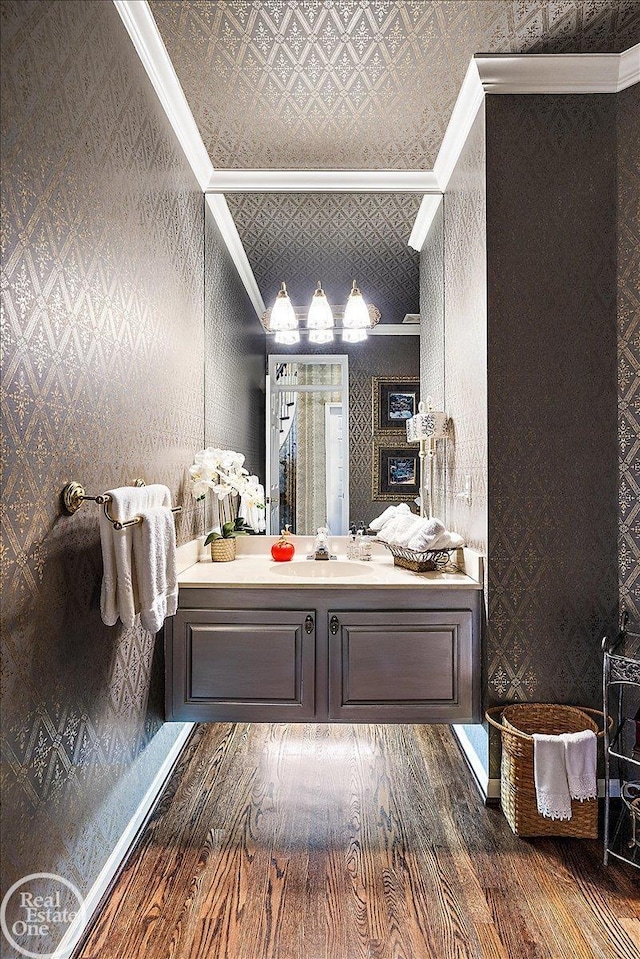 bathroom with wallpapered walls, an ornate ceiling, wood finished floors, crown molding, and vanity