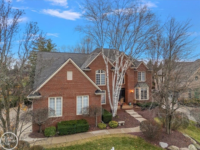 traditional-style home featuring a shingled roof and brick siding