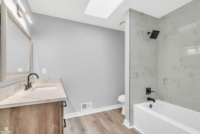 full bathroom featuring a skylight, wood-type flooring, toilet, vanity, and tiled shower / bath