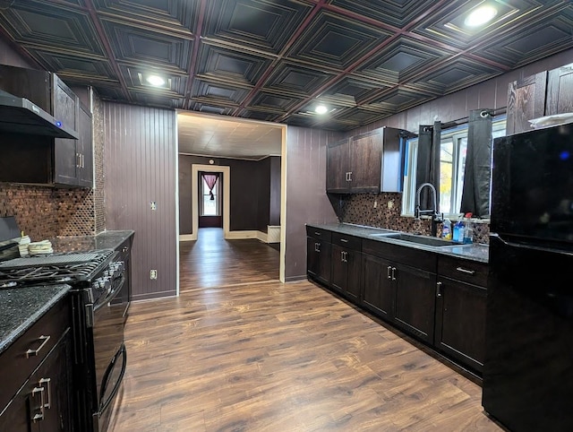 kitchen featuring black appliances, wood-type flooring, sink, wall chimney range hood, and dark brown cabinetry