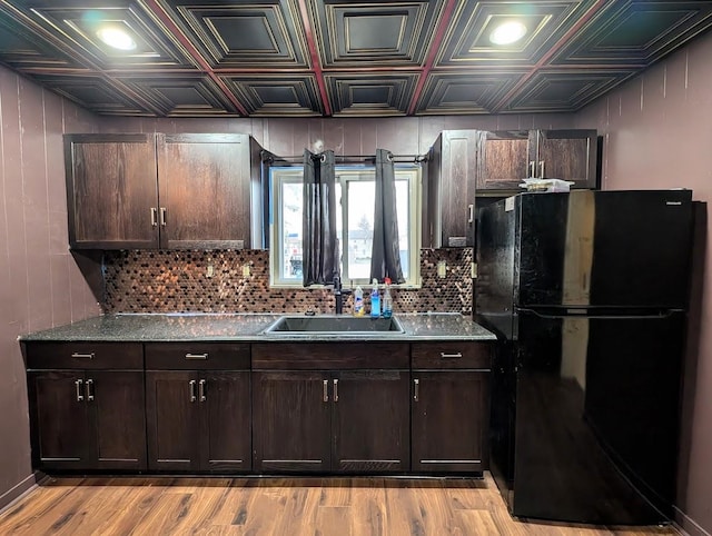 kitchen featuring dark brown cabinetry, sink, black refrigerator, and light hardwood / wood-style flooring