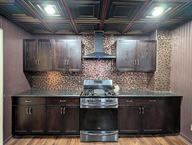 kitchen featuring stainless steel gas stove, dark brown cabinetry, wall chimney range hood, and light hardwood / wood-style flooring