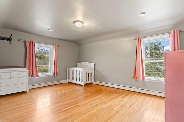 unfurnished bedroom featuring a nursery area, light hardwood / wood-style flooring, and a baseboard radiator