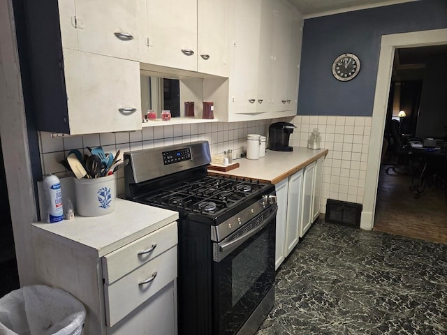 kitchen with stainless steel gas range oven, white cabinets, and tile walls