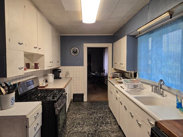 kitchen featuring white cabinets, stainless steel gas stove, dishwasher, and tile walls