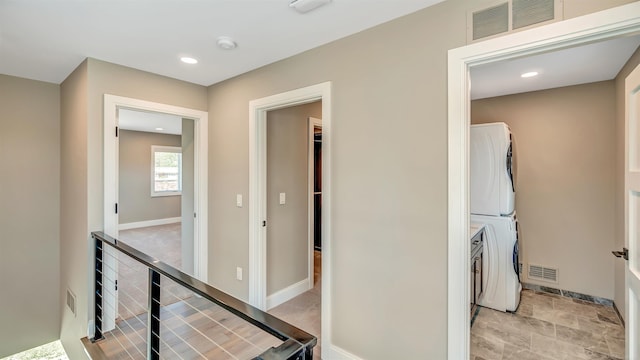 hallway featuring stacked washer and dryer, baseboards, visible vents, and an upstairs landing