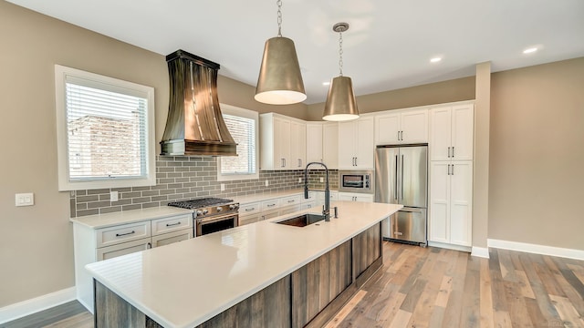 kitchen featuring custom exhaust hood, white cabinets, sink, an island with sink, and premium appliances