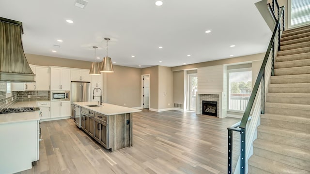 kitchen with custom range hood, light countertops, appliances with stainless steel finishes, open floor plan, and a sink