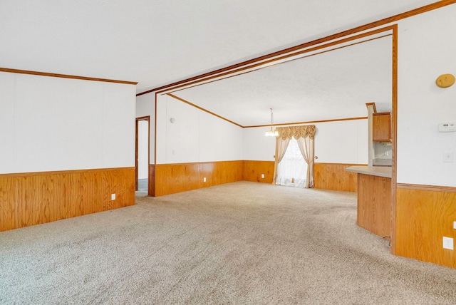 spare room featuring light carpet, wooden walls, ornamental molding, and a notable chandelier