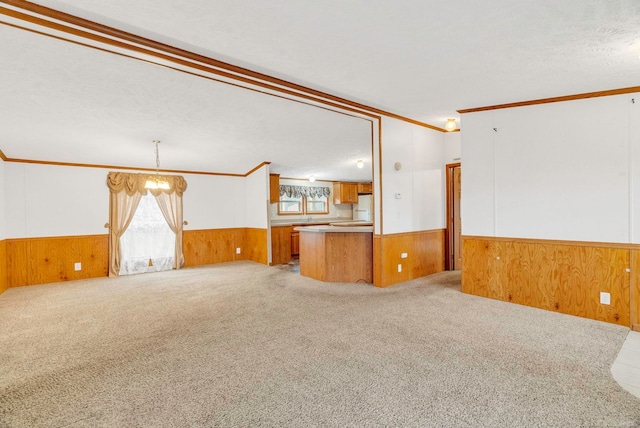 unfurnished living room with light carpet, ornamental molding, a textured ceiling, an inviting chandelier, and wood walls