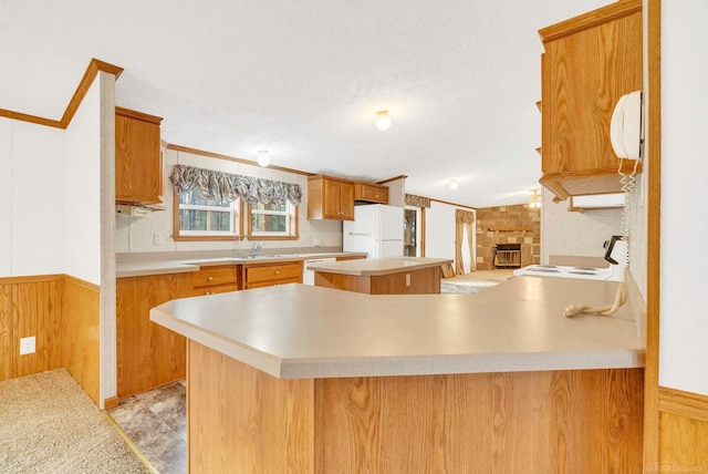 kitchen featuring a center island, wood walls, white appliances, a fireplace, and kitchen peninsula