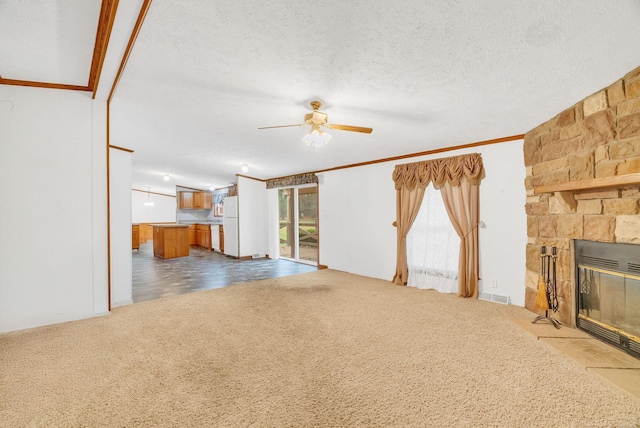 unfurnished living room with a textured ceiling, ceiling fan, crown molding, carpet floors, and a stone fireplace