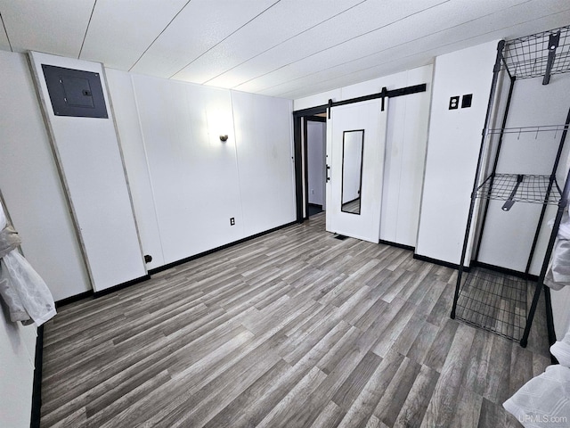 unfurnished bedroom featuring a barn door, light hardwood / wood-style flooring, and electric panel