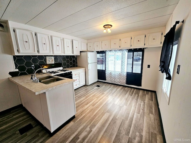 kitchen featuring white cabinets, sink, hardwood / wood-style flooring, white fridge, and kitchen peninsula