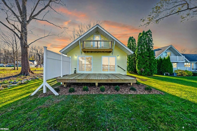 back house at dusk featuring a lawn and a balcony