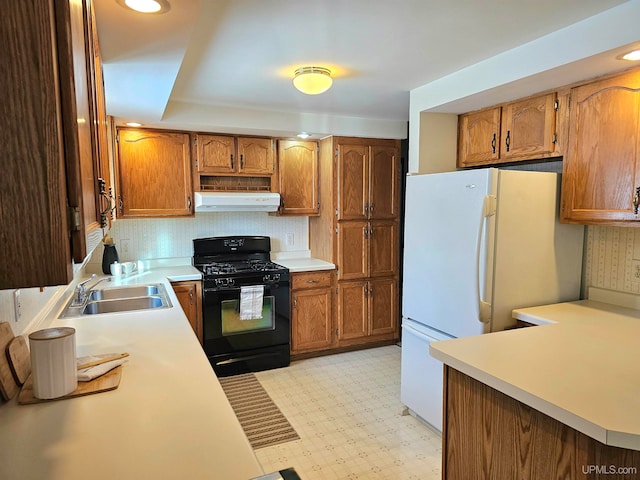 kitchen featuring kitchen peninsula, black range with gas stovetop, sink, and white fridge