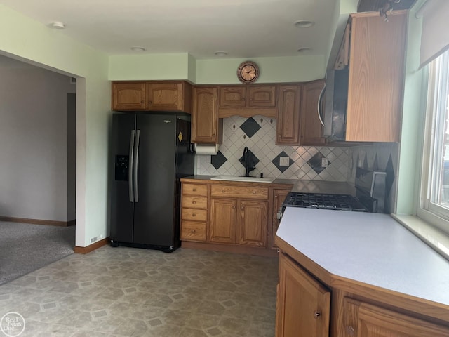 kitchen with black fridge with ice dispenser, backsplash, range with gas cooktop, and sink